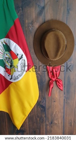Flag of the state of Rio Grande do Sul -Brazil (on fabric), hat and gaucho scarf, on a brown background. Royalty-Free Stock Photo #2183840031