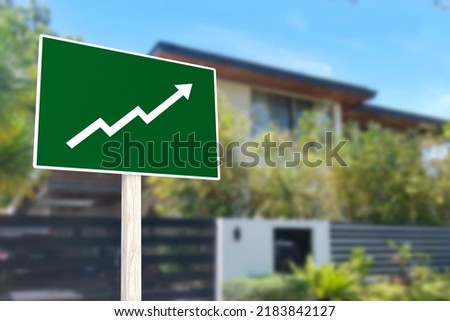 A sign showing an upward arrow in front of a gated house. Concept of increasing home prices and value or a real estate boom. Royalty-Free Stock Photo #2183842127