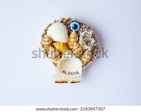Fridge magnet souvenir in shape of sea shells with blue evil eye Nazar Boncuk and inscription Alanya isolated on white background. Travel to Turkey concept. Top view flat lay close up, copy space