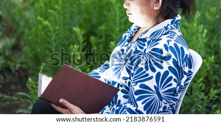 A young Asian woman with black hair sits on a reading chair against a flower garden background.