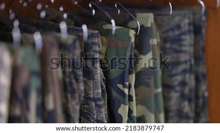 Close-up of collection of military uniform trousers in wardrobe. Camouflage military clothes concept