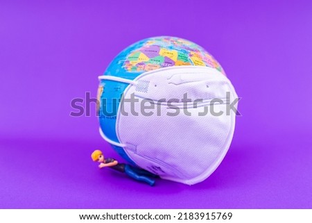 World Planet Earth with face mask protect,miniature toy girl is pressed by the globe on the purple ,veri peri background.World medical concept.