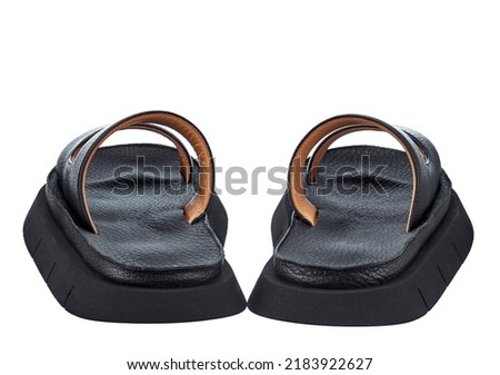 Beautiful pair of black flip-flops made of genuine leather with stripes-straps on top and a massive high sole. Rear view. The trend of the season.