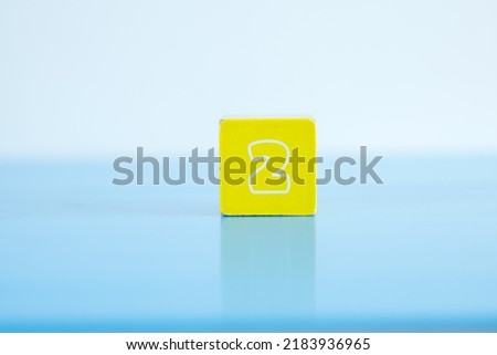 Number digit 2 written on colorful wooden block placing on blue background. 