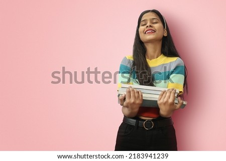 Excited young indian asian girl student posing islolated holding textbooks with love fond of reading or spend free time with books as a hobby and relaxing with closed eyes and chin up.