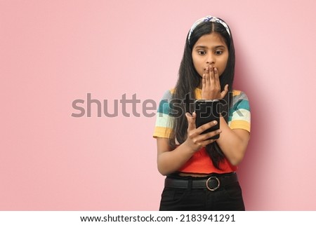 Surprised young Indian Asia girl using mobile phone standing isolated like telephone reader, news, check instagram followers pictures unexpected unbelievable . Mock up copy space.
