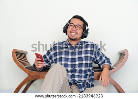 Adult Asian man relaxing while listening music with happy expression Royalty-Free Stock Photo #2183946923