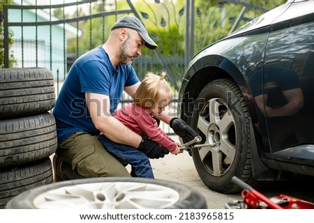 Cute toddler boy helping his father to change car wheels at their backyard. Father teaching his little son to use tools. Active parent of a small child. Royalty-Free Stock Photo #2183965815