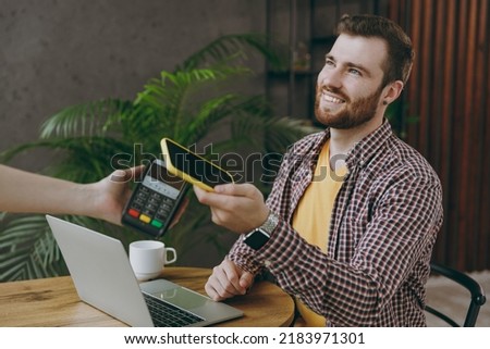 Young man he wear shirt hold wireless bank payment terminal cell phone process acquire credit card payments sit at table in coffee shop cafe rest in free time Freelance mobile office business concept Royalty-Free Stock Photo #2183971301