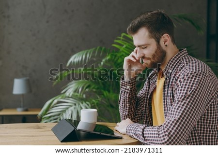 Side view young fun man he wear shirt graphic designer hold work use write draw stylus pc pen sit at table in coffee shop cafe relax rest in free time indoors Freelance mobile office business concept.
