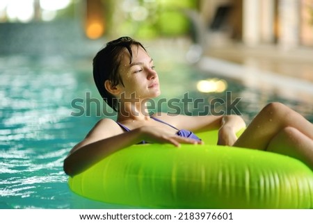Cute young girl playing with inflatable ring in indoor pool. Child learning to swim. Kid having fun with water toys. Family fun in a pool. Activities for family with kids. Royalty-Free Stock Photo #2183976601
