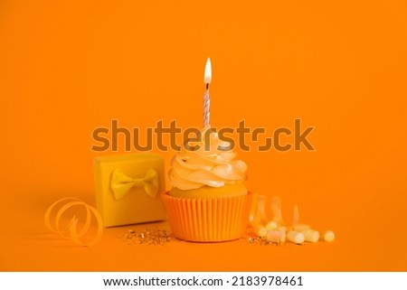 Delicious birthday cupcake with burning candle, marshmallows and gift box on orange background