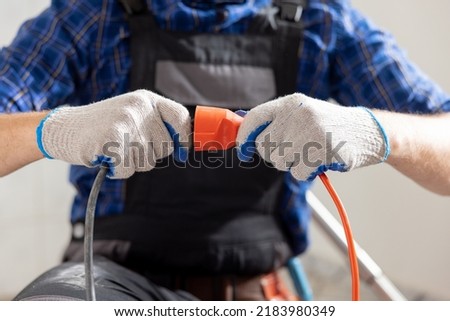 Connecting cables with a plug, extension cord plugging in construction equipment, breakdown, short circuit in house during renovation experienced man in field of electricity repairs electrical. Royalty-Free Stock Photo #2183980349