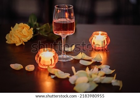 A glass of rose wine, two candles and rose petals on a dark table. Nice evening romantic atmosphere Royalty-Free Stock Photo #2183980955