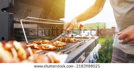 Young man grilling some kind of meats on the gas grill during lovely summer time, food concept Royalty-Free Stock Photo #2183988025