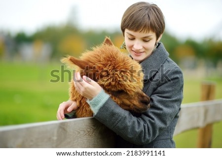 Cute young girl stroking an alpaca at a farm zoo on autumn day. Child feeding a llama on an animal farm. Kid at a petting zoo at fall. Active leisure children outdoor. Royalty-Free Stock Photo #2183991141
