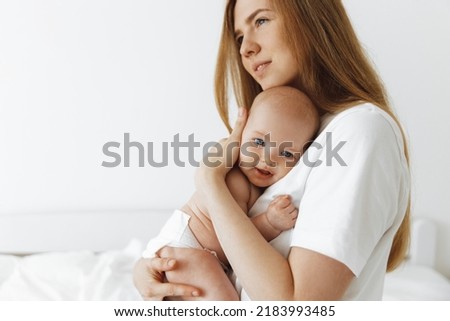 young caring mother hugged her little daughter, pressing her to her chest. Beautiful woman holding a newborn baby in her arms at home. Smiling mother hugging a small newborn baby showing love 