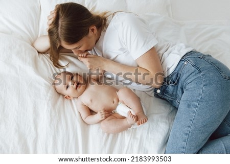 young mother with her little daughter, dressed in pajamas, relaxing in bed on the weekend and playing in bed together, lazy morning, warm and cozy scene. Pastel colors, top view.