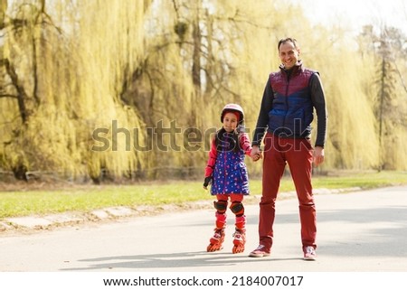 A father teaching his daughter roller skating in a park on summer day. Happy week-end. Father's day