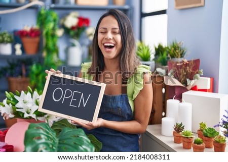 Hispanic young woman working at florist with open sign smiling and laughing hard out loud because funny crazy joke. 
