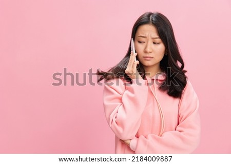 Confused unhappy cute Asian student young lady in pink hoodie sweatshirt get sad news from call posing isolated on over pink studio background. Good offer. Gadget addiction Social Media concept