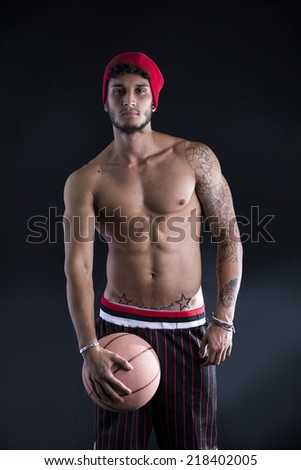 Young athletic man on dark background holding basketball ball, looking at camera