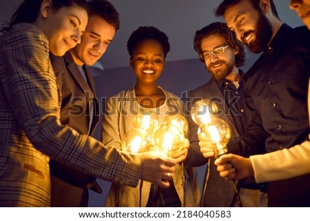 Multiracial business team sharing ideas, inspiration and creative energy with each other. Diverse group of happy people looking at bright Edison light bulbs in their hands. Teamwork, success concept Royalty-Free Stock Photo #2184040583