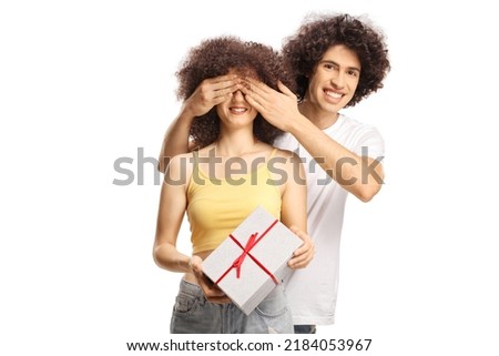 Boyfriend surprising a girlfriend with a present and covering her eyes isolated on white background

