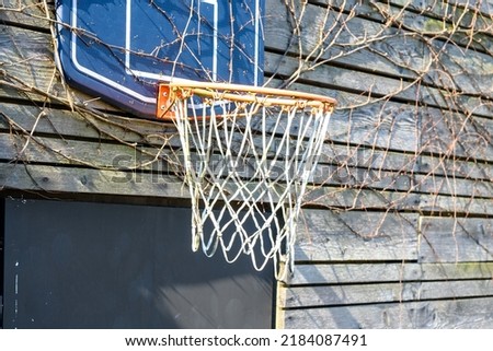 Basketball hoop on the garage. sunlight. Outdoor sports. Healthy lifestyle. Wood wall lifestyle. A basketball basket installed in the garage by the house. Basketball hoop overgrown with dried  ivy. Royalty-Free Stock Photo #2184087491