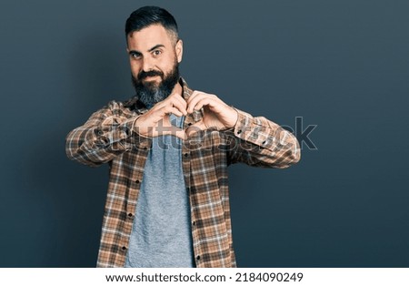 Hispanic man with beard wearing casual shirt smiling in love doing heart symbol shape with hands. romantic concept. 