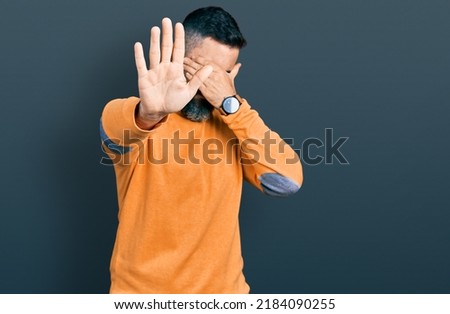 Hispanic man with beard wearing casual winter sweater covering eyes with hands and doing stop gesture with sad and fear expression. embarrassed and negative concept. 