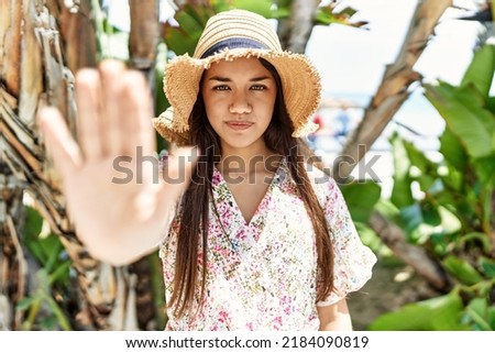 Young brunette woman outdoors on a sunny day of summer smiling happy doing ok sign with hand on eye looking through fingers 