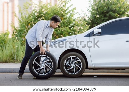 Handsome Asian young man holding spare wheel against for changing flat tire on the road. Royalty-Free Stock Photo #2184094379
