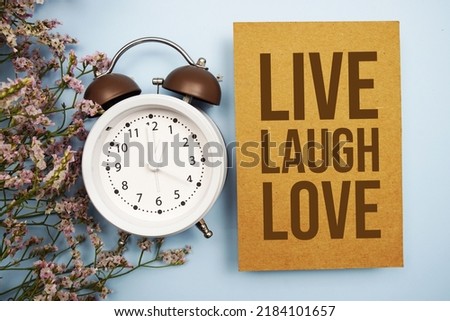 Live Laugh Love written on paper card with flower and alarm clock on blue background