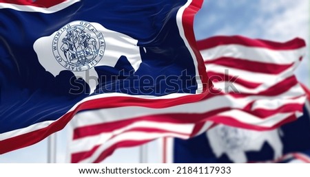 The Wyoming state flag waving along with the national flag of the United States of America. Wyoming is a state in the Mountain West subregion of the Western United States Royalty-Free Stock Photo #2184117933
