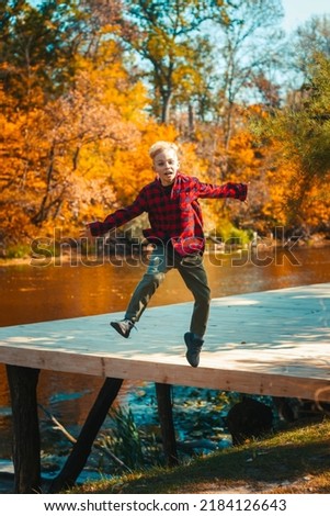 A young handsome boy jumps on a panton cheerful in autumn in the park by the lake