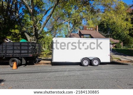 A landscaping truck with a long white enclosed trailer trailer seen on a shady residential asphalt street Royalty-Free Stock Photo #2184130885