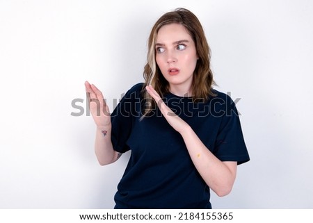 Displeased young caucasian woman wearing black T-shirt over white background keeps hands towards empty space and asks not come closer sees something unpleasant