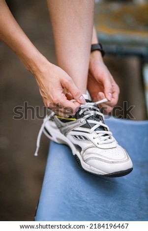 Closeup photo of athlete girl's legs in sneakers, she ties shoes in summer on a stadium chair outside with fitness tracker. Happy young female sport, workout, travelling, healthy lifestyle concept
