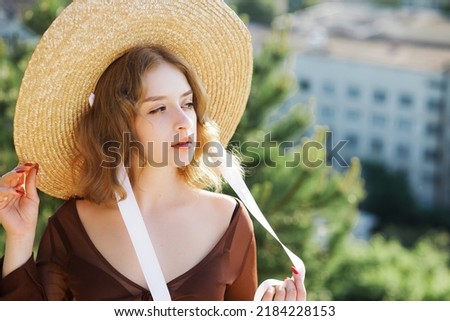 Portrait of a beautiful young girl in a straw hat, posing against the background of the city from an observation deck.