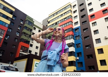 Portrait of a happy caucasian teenage girl with pink braids against the background of urban high-rise buildings.Summer concept.Generation Z style.Selective focus.