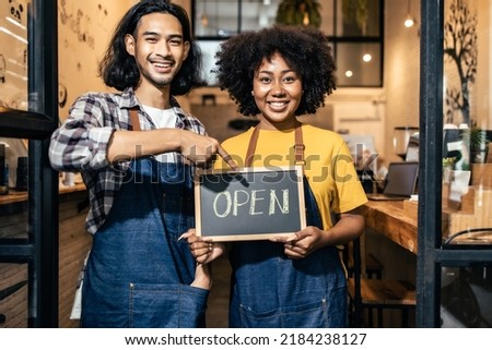 Young  couple asian man and african woman manager in restaurant with digital tablet or notebookWoman coffee shop owner with face mask hold open sign .Small business concept.