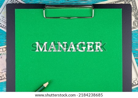 MANAGER - word (text) and money bills, dollars on a green background notepad, pencil, wooden table. Business concept: buy, sell, commerce (copy space).