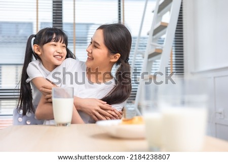 Asian  family enjoying breakfast at living room. little girl daughter sitting on table, drinking milk with smiling father and mother in morning. Happy family at home. Royalty-Free Stock Photo #2184238807