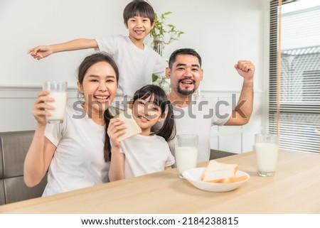 Asian  family enjoying breakfast at living room. little girl daughter sitting on table, drinking milk with smiling father and mother in morning. Happy family at home. Royalty-Free Stock Photo #2184238815