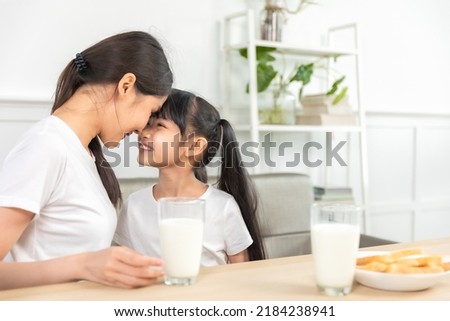 Asian  family enjoying breakfast at living room. little girl daughter sitting on table, drinking milk with smiling father and mother in morning. Happy family at home. Royalty-Free Stock Photo #2184238941