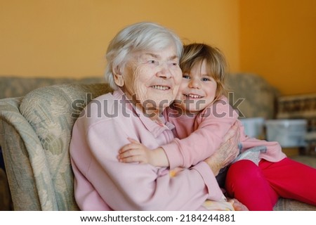 Beautiful toddler girl and great-grandmother hugging together at home. Cute child and senior woman having fun together. Happy family indoors