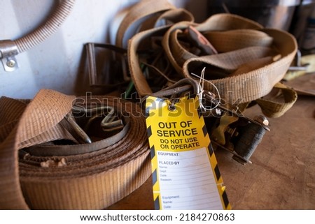 Safe workplaces practices yellow out of service warning tag sign placing on damaged faulty unsafe to use truck tie down strap load restraint ratchet webbing   Royalty-Free Stock Photo #2184270863