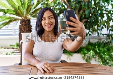 Hispanic brunette woman sitting taking selfie at the terrace
