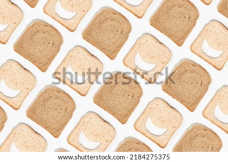 Slices of whole-grain brown toast bread and white bread with smile-shaped holes on isolated white background. High-carb food concept or food for digestion problems. Minimal flat lay. Top view pattern. Royalty-Free Stock Photo #2184275375